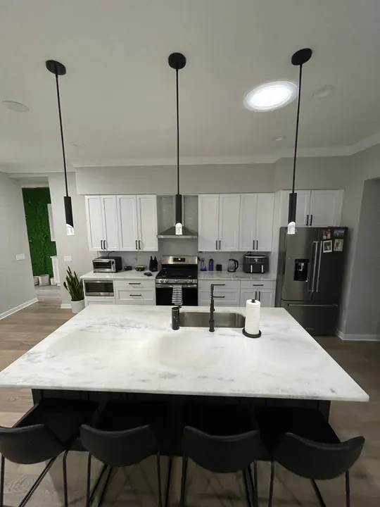 Remodeled kitchen with white shaker cabinets, black pendant lights over a marble island and a matte-black faucet