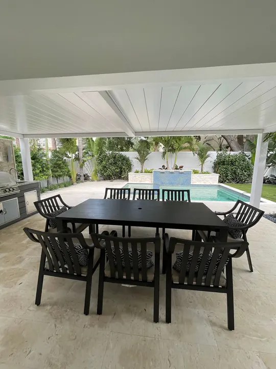 Covered patio with a newly assembled black outdoor dining table and chairs beside a pool
